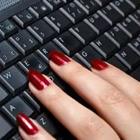 Los dedos de una persona con las uñas pintadas de rojo en un teclado negro