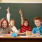 Cuatro niños en un aula levantando las manos